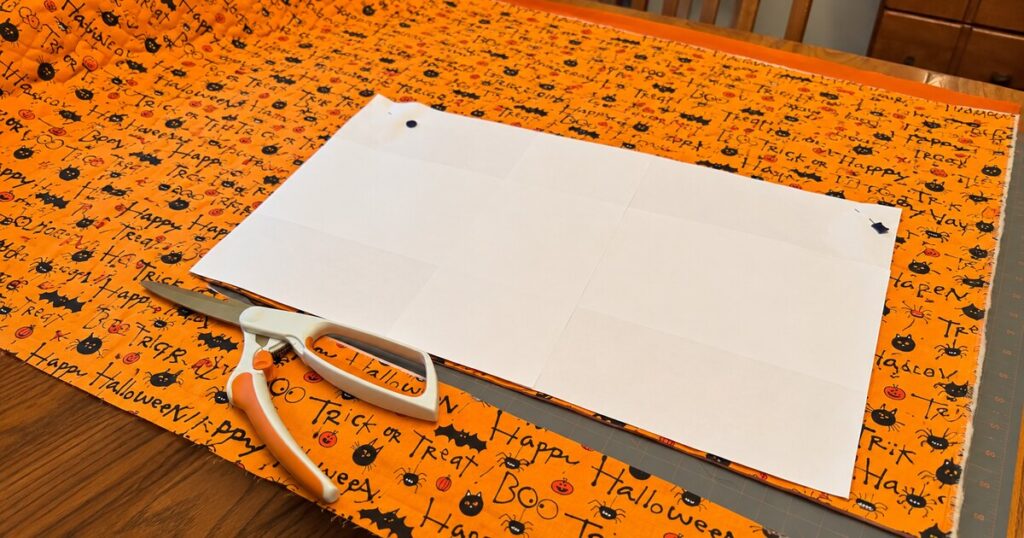 Halloween fabric quilted on a longarm with a paper placemat template and scissors ready for cutting